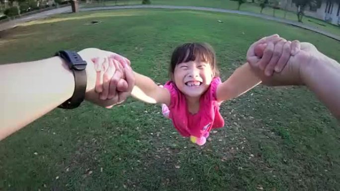 父亲在公园里旋转他的小女儿，孩子对着镜头微笑的视点镜头
