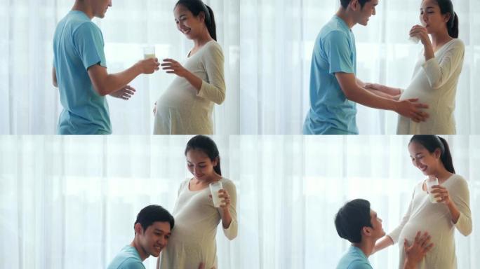 年轻人正在倾听并亲吻他美丽的怀孕妻子的肚子并微笑。怀孕/出生