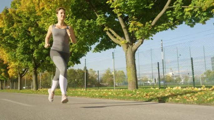 低角度: 一个年轻的女性慢跑者沿着充满活力的人行道奔跑的电影镜头