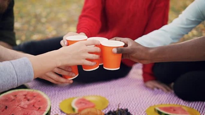 男女朋友拿着饮料的慢动作，然后碰杯，坐在公园的毯子上玩得开心，在秋天一起野餐。
