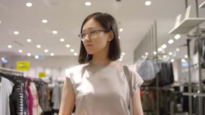 年轻的亚洲妇女走过服装店，环顾四周