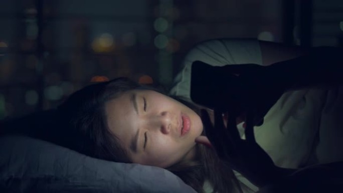 bokeh light city夜间在床上使用智能手机的亚洲女性