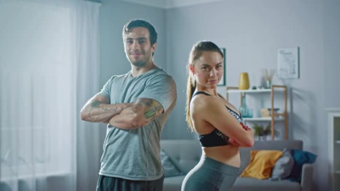 肌肉发达的运动男人和穿着运动服的美丽健身女人在他们明亮宽敞的公寓里自信地摆姿势，室内简约。