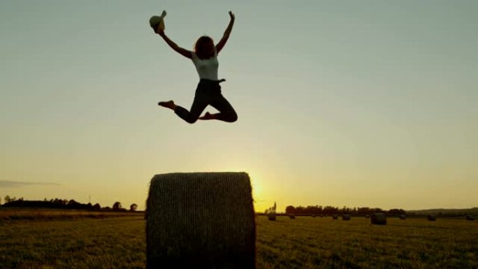 日落时，Slo Mo女士无忧无虑的女人在田园诗般的乡村田野上跳上干草草