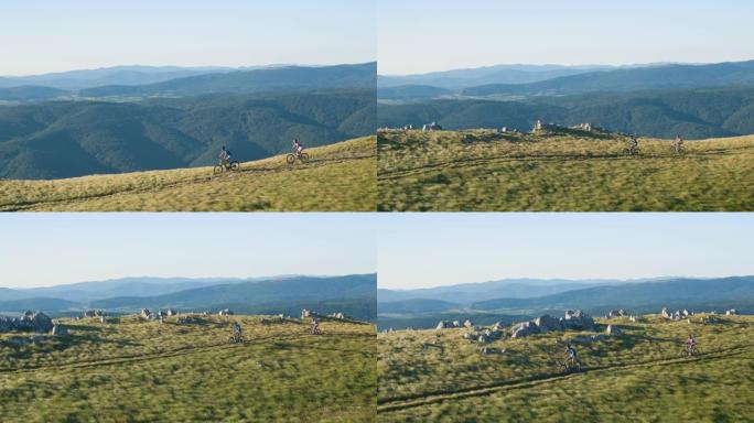 空中: 山地自行车夫妇沿着俯瞰山谷的草地小径加速行驶。