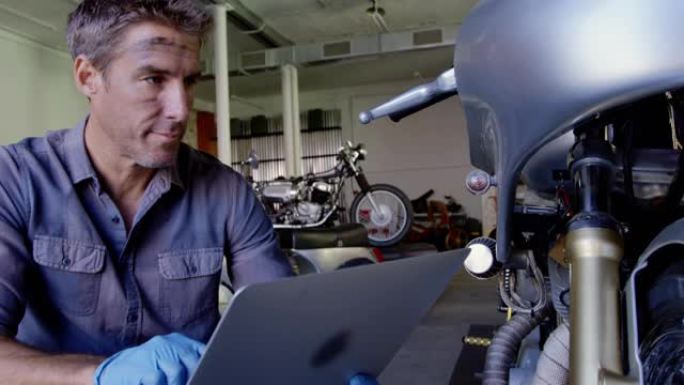 在摩托车维修车库使用笔记本电脑的男性机械师4k