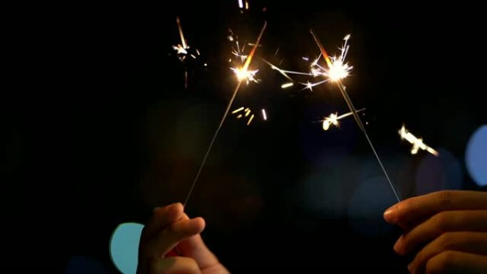 4K慢镜头手持式烟花在夜晚闪烁，以散景城市为背景，庆祝新年快乐和党的概念