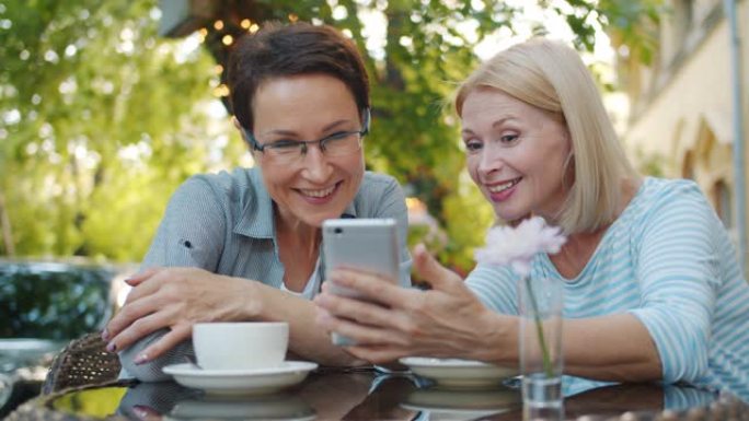 在露天咖啡馆微笑中使用智能手机的漂亮女人的慢动作