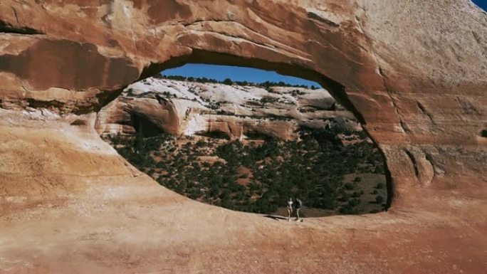 无人机在亚利桑那州国家公园山脉的中间与两名游客一起飞过巨大的拱门岩层。