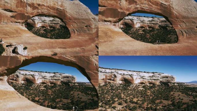 无人机在亚利桑那州国家公园山脉的中间与两名游客一起飞过巨大的拱门岩层。