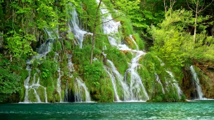 可爱的瀑布，有许多小瀑布，周围是丰富的绿色植物，流入克罗地亚十六湖国家公园的绿松石色湖泊。4K