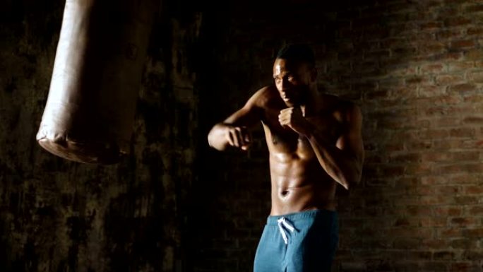 一个非裔美国人在老式健身房训练，用拳头打他的拳击袋拳头。