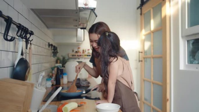 千禧一代的母亲用女儿的帮助手在家做饭煎蛋卷在厨房准备早餐。