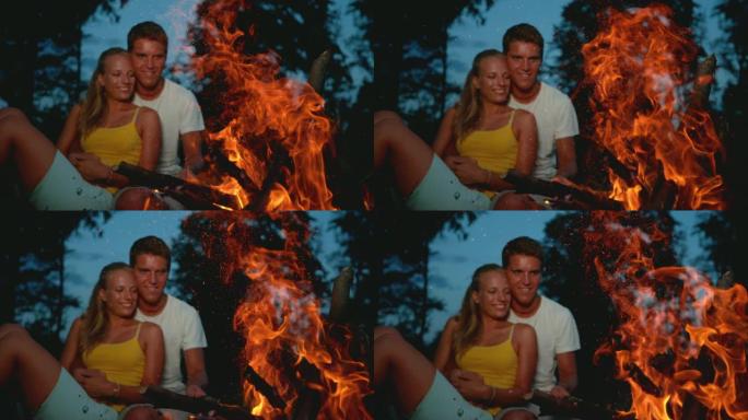 特写: 微笑的年轻夫妇在篝火旁享受一个平静的夏日夜晚。