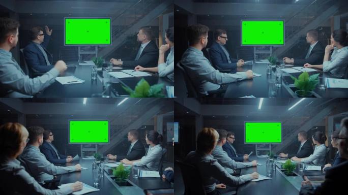 深夜在公司会议室: 董事会，高管和商人坐在谈判桌旁，交谈并使用绿色模拟屏幕墙电视进行视频电话会议。