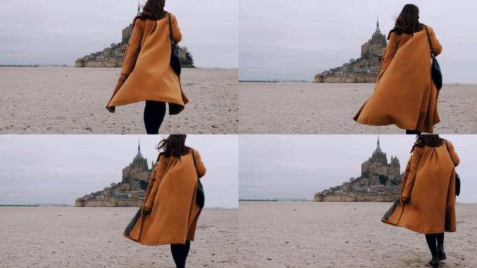 中后视镜头，优雅快乐的博客作者女人走在史诗圣米歇尔山城堡的海底沙滩上慢动作