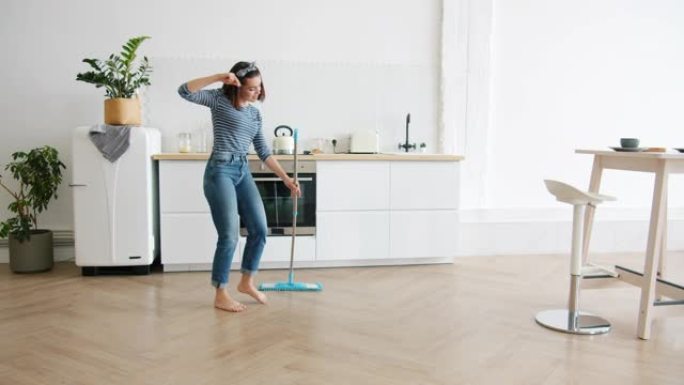 快乐的年轻女子用拖把洗地板，在厨房里跳舞