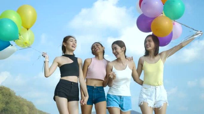 时髦的朋友带着快乐的心情抱着五颜六色的气球走在海滩上。有派对庆祝概念的人。4k分辨率。慢动作镜头。