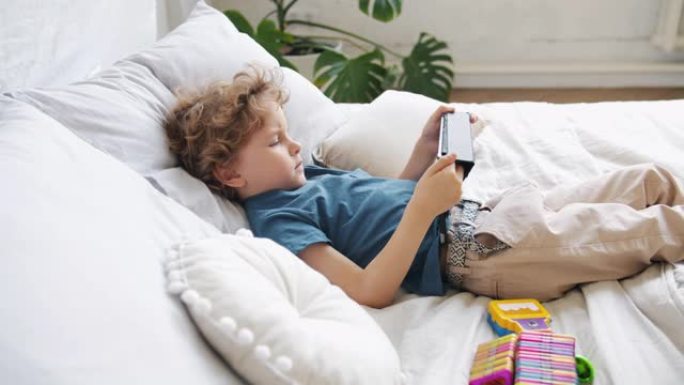 小孩用平板电脑独自躺在床上看动画片在家放松