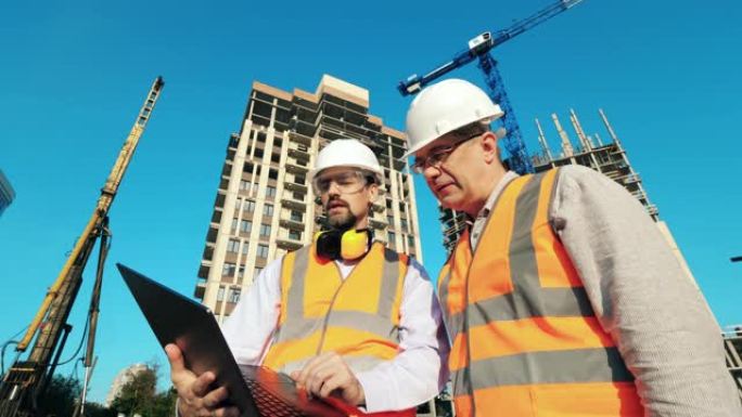 工作工程师，建筑建筑师站在建筑工地上讨论使用笔记本电脑的施工计划。