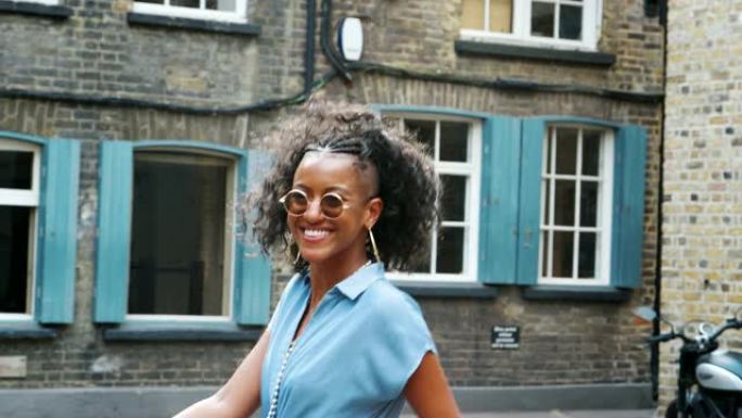 穿着蓝色衬衫连衣裙和太阳镜的时尚年轻黑人女性走在街上，转向镜头，向后看