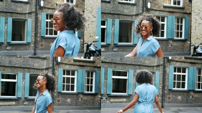 穿着蓝色衬衫连衣裙和太阳镜的时尚年轻黑人女性走在街上，转向镜头，向后看