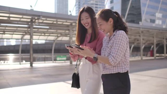 两名亚洲女商人在步行上班时使用智能手机