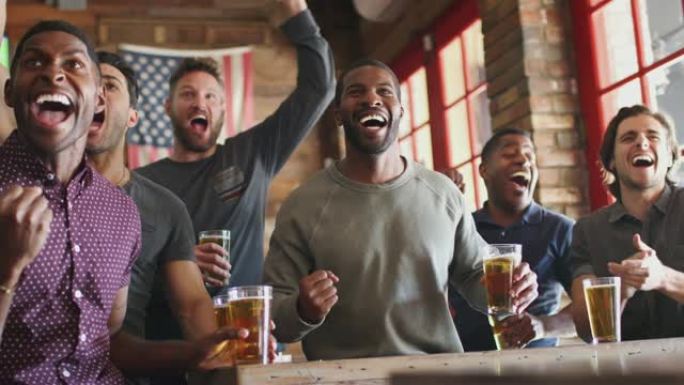 一群男性朋友在体育酒吧的屏幕上观看比赛时庆祝