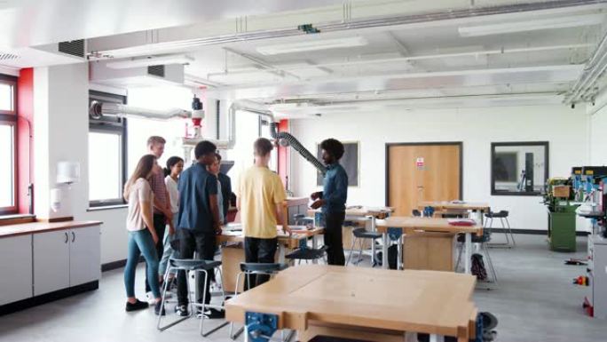 在设计与技术课中，老师与一群站在工作台周围的高中生交谈