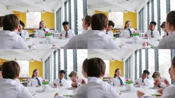 一群穿着制服的高中生围坐在桌子旁，在自助餐厅吃午餐