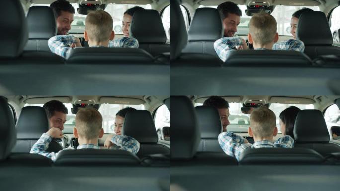 快乐的父母在坐在汽车里的陈列室里和小男孩聊天，选择汽车
