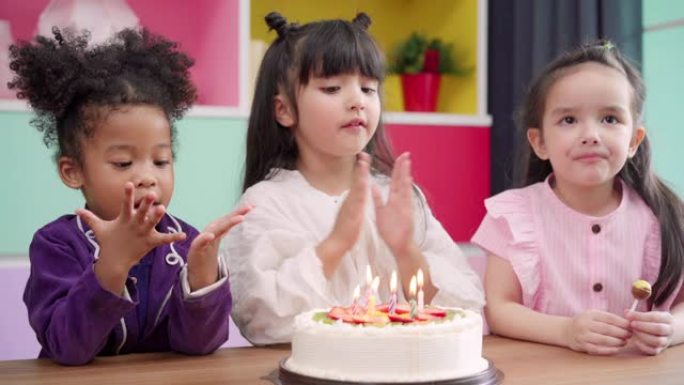 一群孩子在教室里庆祝生日聚会，多民族的年轻男孩和女孩快乐地许愿在学校的生日蛋糕上吹灭蜡烛。孩子们在学