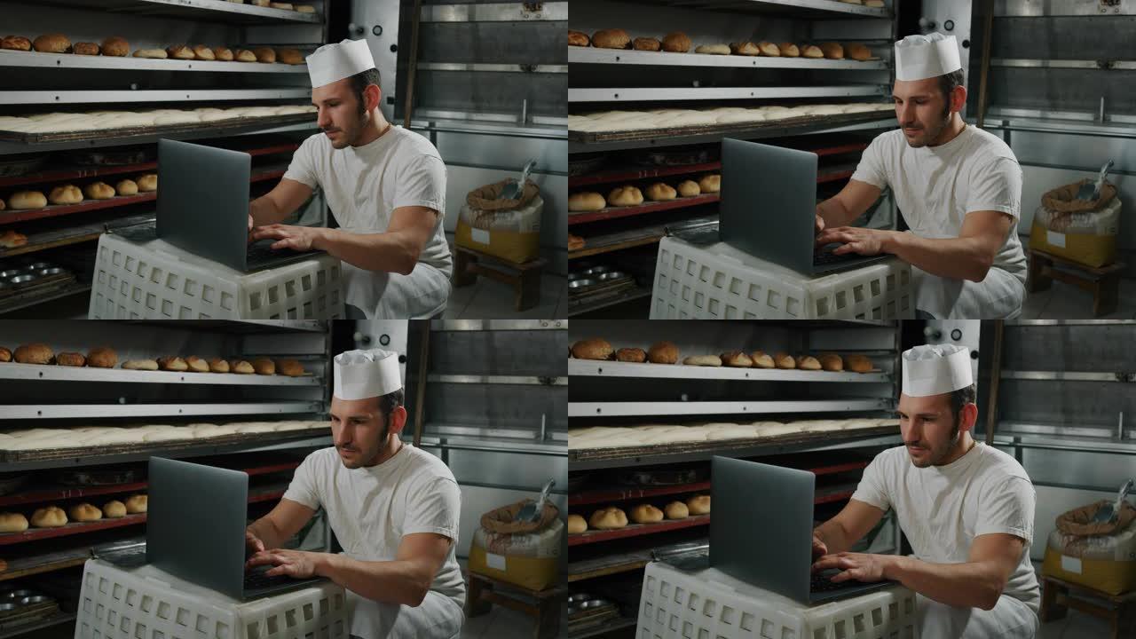 英俊的年轻面包师学生的慢动作使用笔记本电脑在面包店进行在线学习和学习课程，背景是面包和烤箱