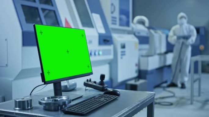 工厂洁净室: 桌上的个人电脑上显示绿屏色键显示。在背景数控机械中，专业人员在生产线上使用机械臂。放大