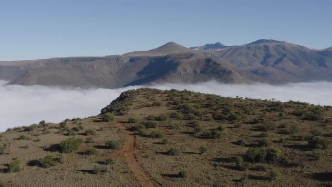 4K空中倾斜向上的视野，一个safari 4x4游戏驾驶车辆行驶在一个砾石路美丽的山景在背景