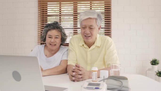 亚洲老年夫妇在客厅使用笔记本电脑与医生讨论药物信息，夫妇躺在家里的沙发上一起使用时间。老年人家庭健康