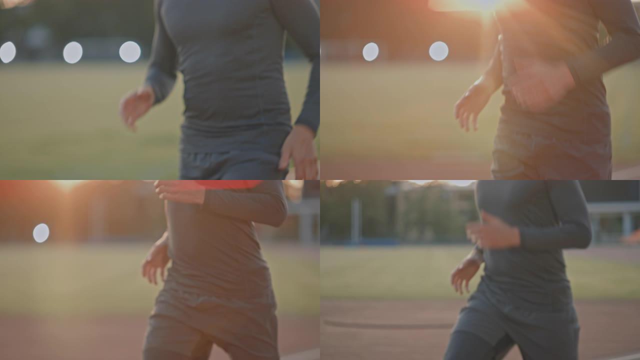 穿着灰色衬衫和短裤的运动健美男子在体育场慢跑。在一个温暖的夏日下午，他跑得很快。运动员做他的常规运动