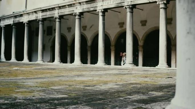 快乐的旅游女人在意大利威尼斯的美丽的古建筑露台上散步，那里有古董柱子。