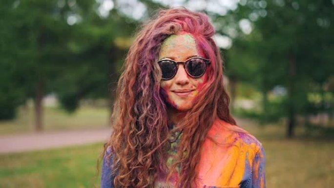 Holi holiday的美丽女孩戴着墨镜站在户外，脸上和头发覆盖着鲜艳的古拉尔颜料。青年和传统概念