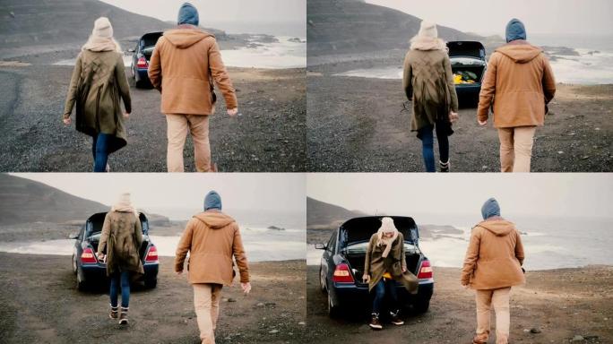 年轻幸福的夫妇开车旅行。迷人的男人和女人走到冰岛黑海滩附近的车辆上。