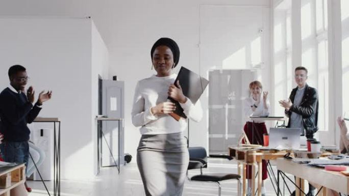 快乐微笑的年轻非洲女经理带着一个盒子进入新办公室，受到同事慢动作红色史诗的欢迎。