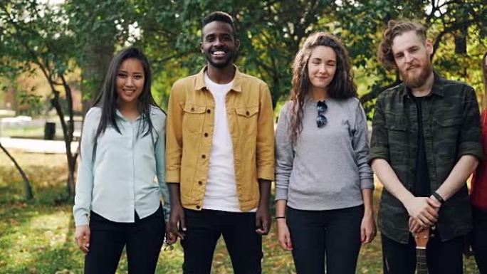 多种族学生群体的慢动作肖像女孩和男孩一起站在户外，带着快乐的微笑看着相机。自然和友谊概念。