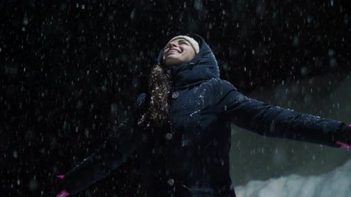 当雪从天而降时，一个美丽的女人在夜晚停在灯光下，开始玩耍，呼吸着干净的空气，在大自然中跳舞。