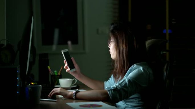 4k镜头迷人的亚洲女人的场景工作到很晚才能在桌子前完成工作在黑暗中的工作场所的电脑显示器桌面上的快乐