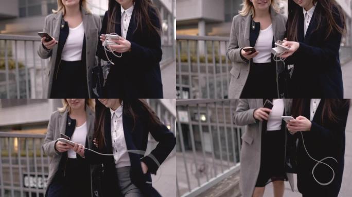 两名商业女性在城市里散步时使用智能手机
