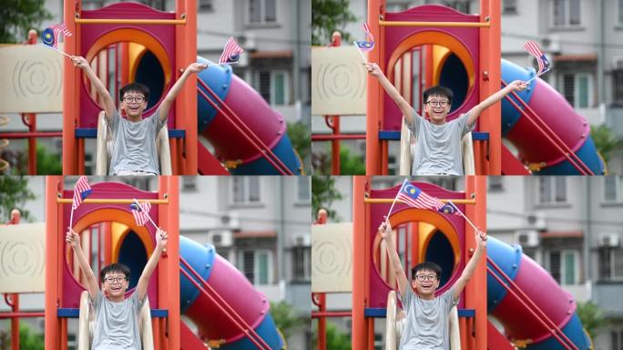 一个亚洲华人小男孩在儿童操场上举着马来西亚国旗