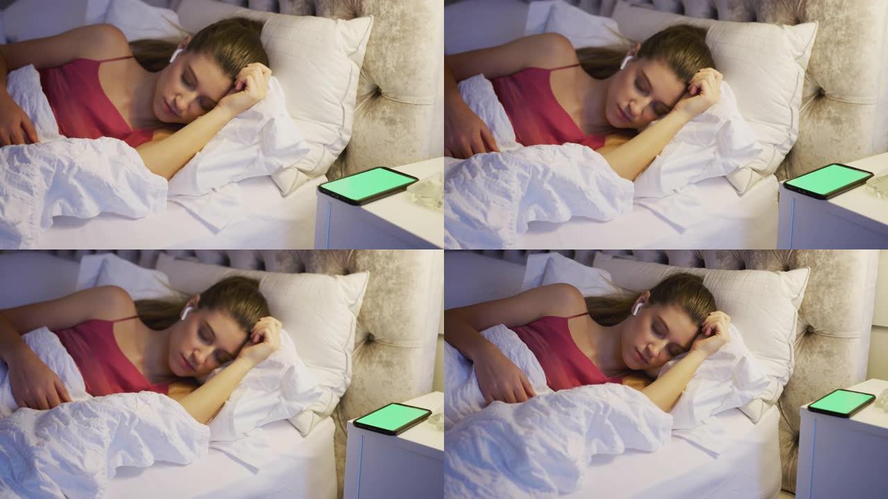 睡在床上的女人戴着无线耳机连接到床头柜上的手机