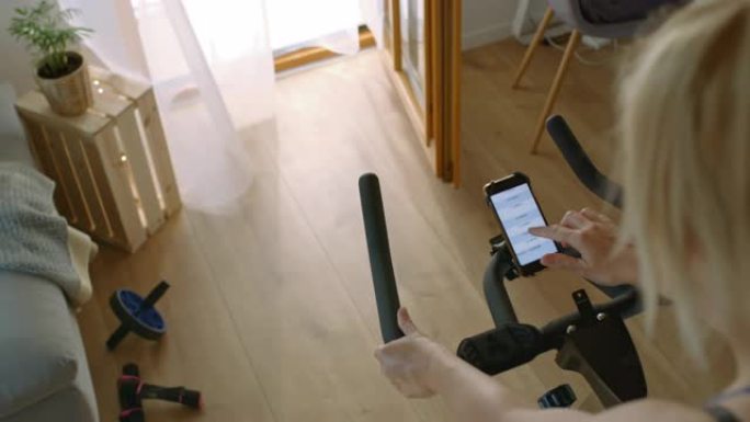 SLO MO女人在家里的健身车上锻炼时使用手机