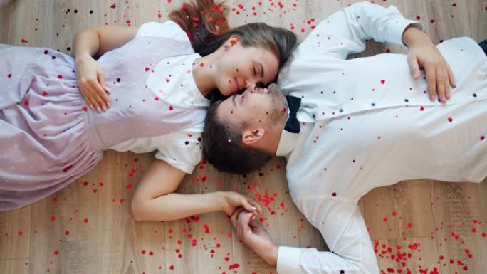 美丽的夫妇面对面躺在地板上，心形五彩纸屑掉下来