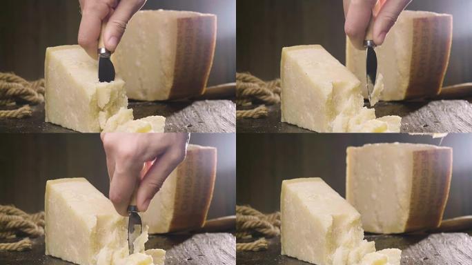 帕尔马干酪组合物，放在木制砧板上。一只手拿着刀，折断几块来品尝质量。